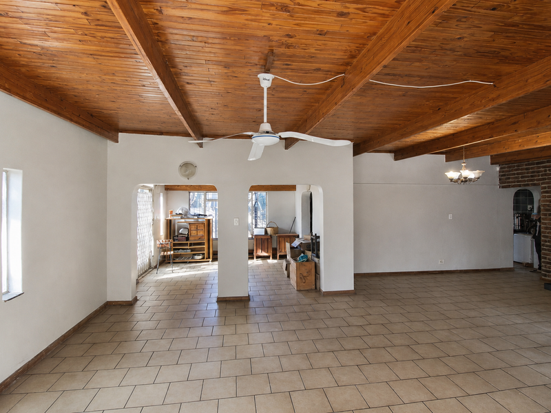Spacious open-plan living area featuring a high exposed timber beam ceiling, tiled flooring, and a distinctive exposed brick feature wall.