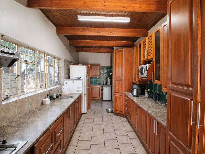 A spacious kitchen featuring timber beam ceilings, extensive wooden cabinetry, laminate countertops, and tiled flooring, offering a functional layout with ample storage space.