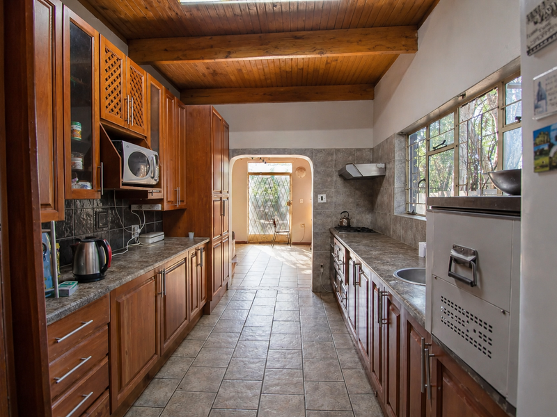 A functional kitchen featuring extensive wooden cabinetry, laminate countertops, built-in appliances, and exposed wooden ceiling beams, leading to an exterior doorway.
