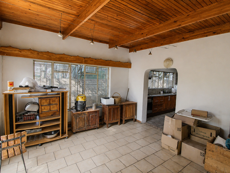 Open-plan living area featuring a timber-clad ceiling with exposed beams, tiled flooring, and an arched transition leading into the kitchen space.