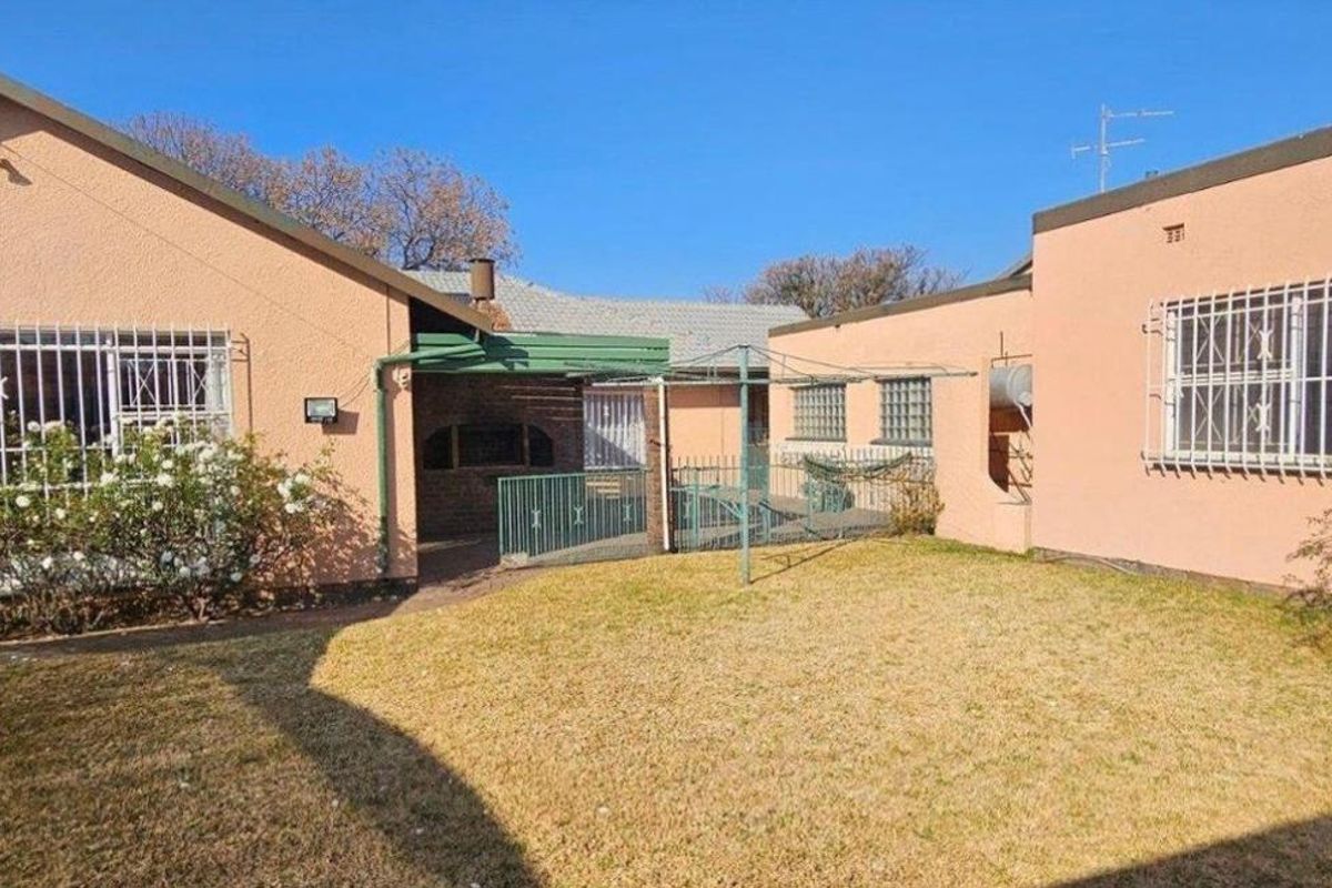 Rear view of the property featuring a lawn, covered patio area with a built-in braai, and security bars on windows.