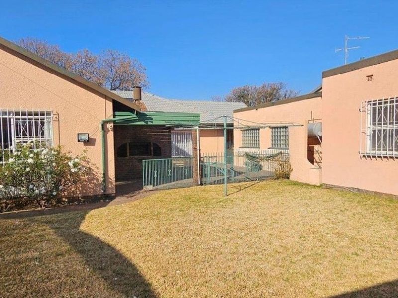 Rear view of the property featuring a lawn, covered patio area with a built-in braai, and security bars on windows.