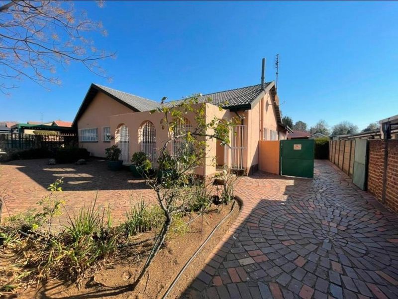 Front exterior view of a single-story house featuring a tiled roof, arched entrance porch, and extensive brick-paved driveway and courtyard area.