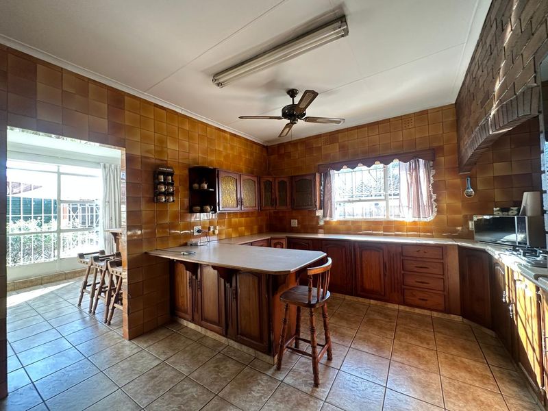 A spacious kitchen featuring extensive wooden cabinetry, tiled splashbacks, a breakfast counter, and direct access to an adjacent sunroom area.