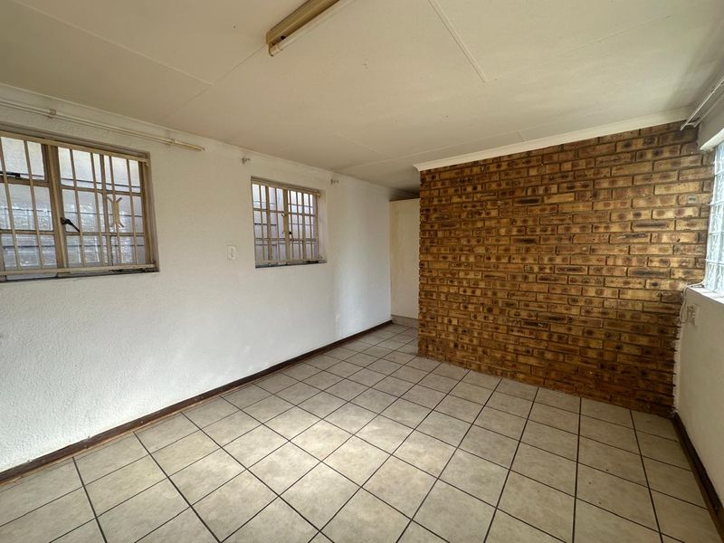 An empty living area featuring tiled flooring, an exposed brick feature wall, and windows fitted with security bars.