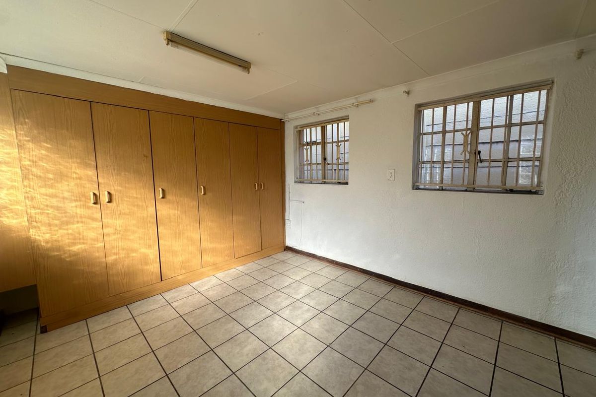 An empty bedroom featuring built-in wooden cupboards, tiled flooring, and windows fitted with security bars.