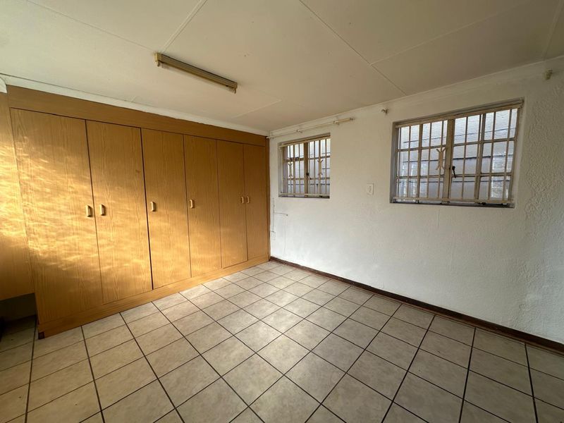 An empty bedroom featuring built-in wooden cupboards, tiled flooring, and windows fitted with security bars.