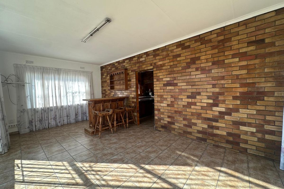 Living area featuring a prominent exposed brick wall, ceramic tiled flooring, and a built-in bar area, offering potential for modern renovation.