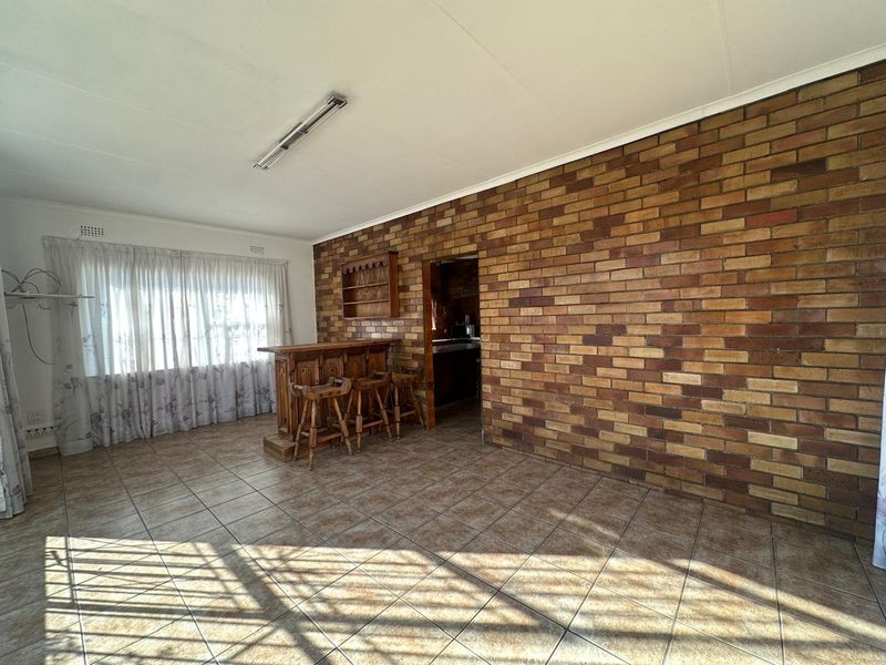 Living area featuring a prominent exposed brick wall, ceramic tiled flooring, and a built-in bar area, offering potential for modern renovation.