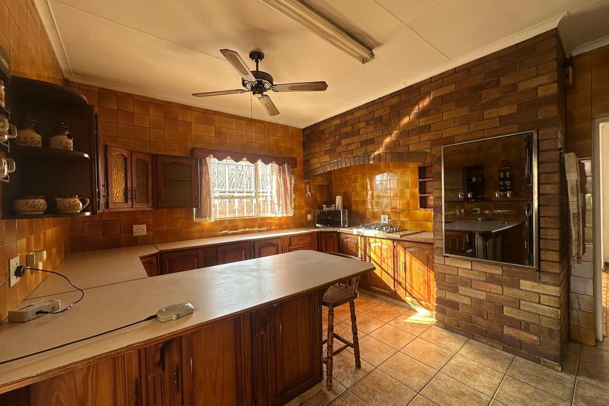 A spacious kitchen featuring traditional wooden cabinetry, a brick feature wall, built-in cooking appliances, and tiled surfaces throughout.