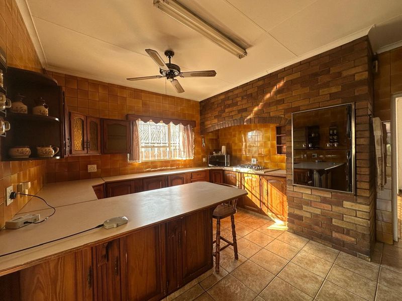A spacious kitchen featuring traditional wooden cabinetry, a brick feature wall, built-in cooking appliances, and tiled surfaces throughout.