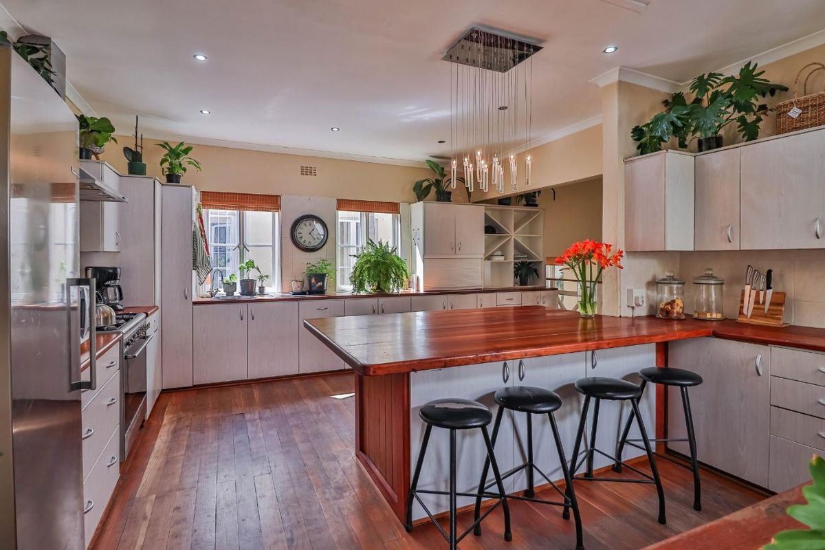 Spacious kitchen featuring a large wooden island, ample built-in cabinetry, stainless steel appliances, and warm hardwood flooring under recessed and pendant lighting.