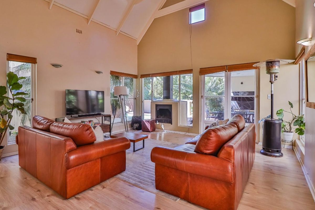 Spacious living room featuring a high vaulted ceiling, timber flooring, a built-in fireplace, and large sliding glass doors providing access to the outdoor area.