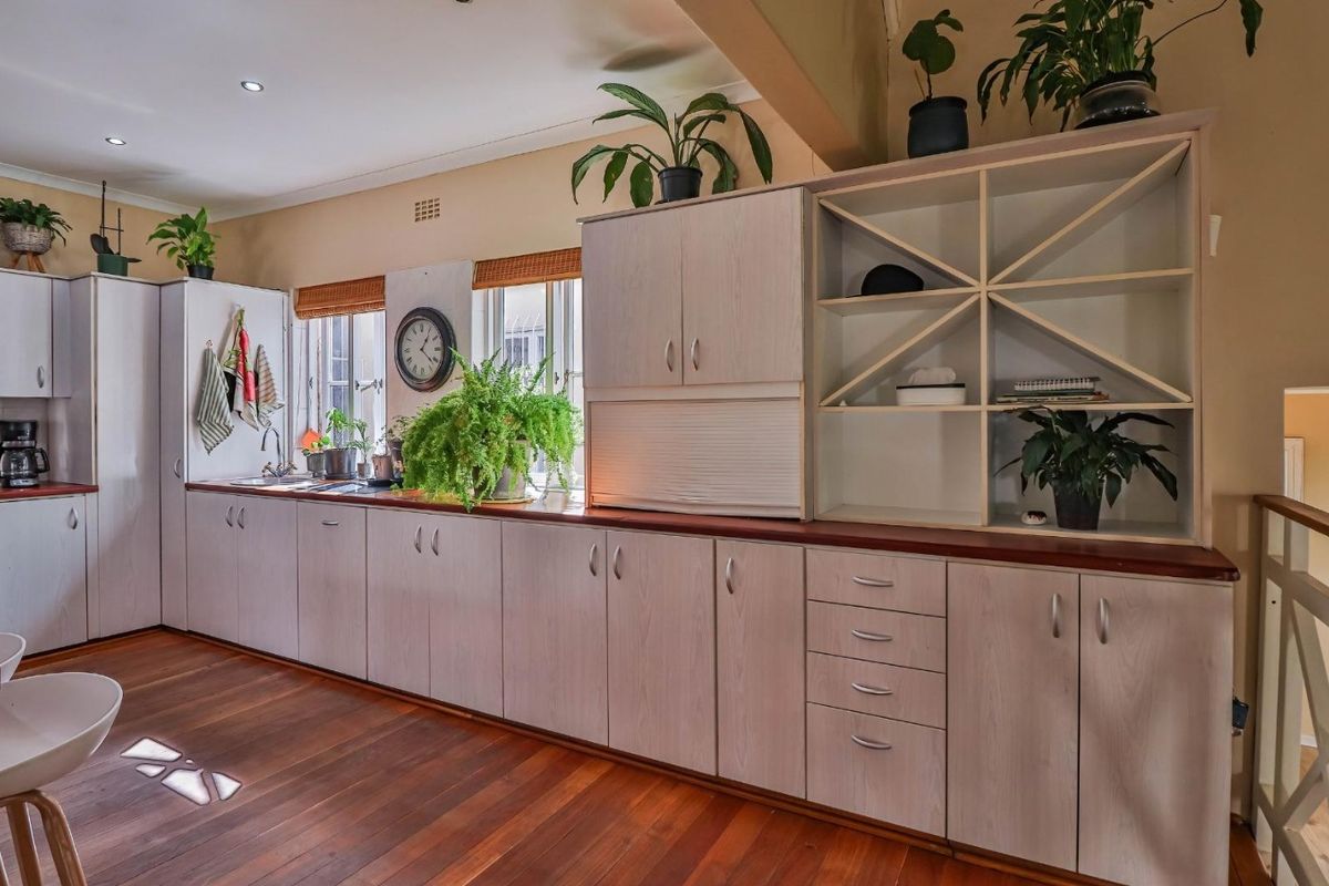 A functional kitchen featuring extensive light-toned built-in cabinetry, dark laminate countertops, a stainless steel sink, and warm timber flooring.