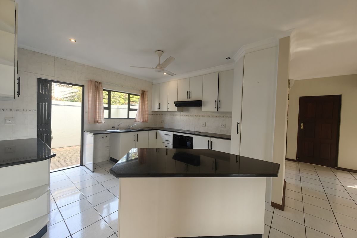 A clean, functional kitchen featuring white cabinetry, dark granite countertops, tiled flooring, and direct access to an outdoor patio area.