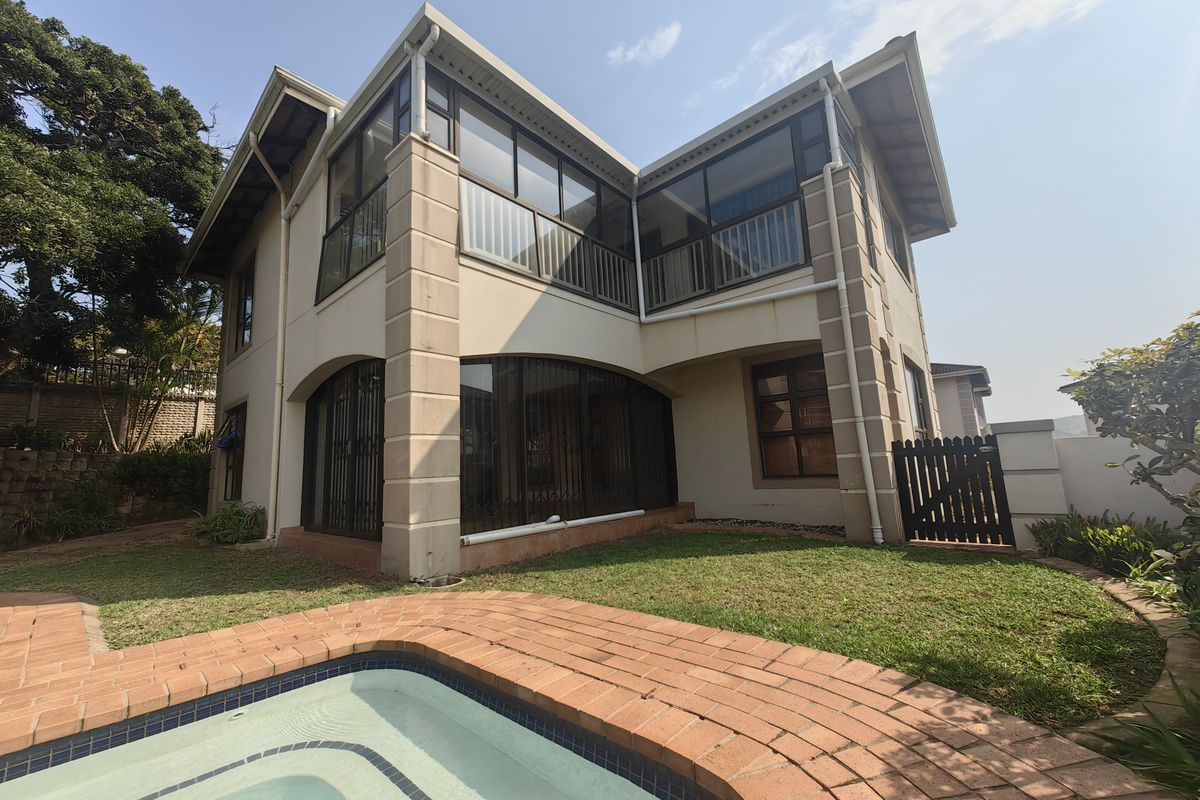 Rear view of a two-story townhouse featuring a swimming pool with brick coping, an enclosed upper balcony, and a private garden area.