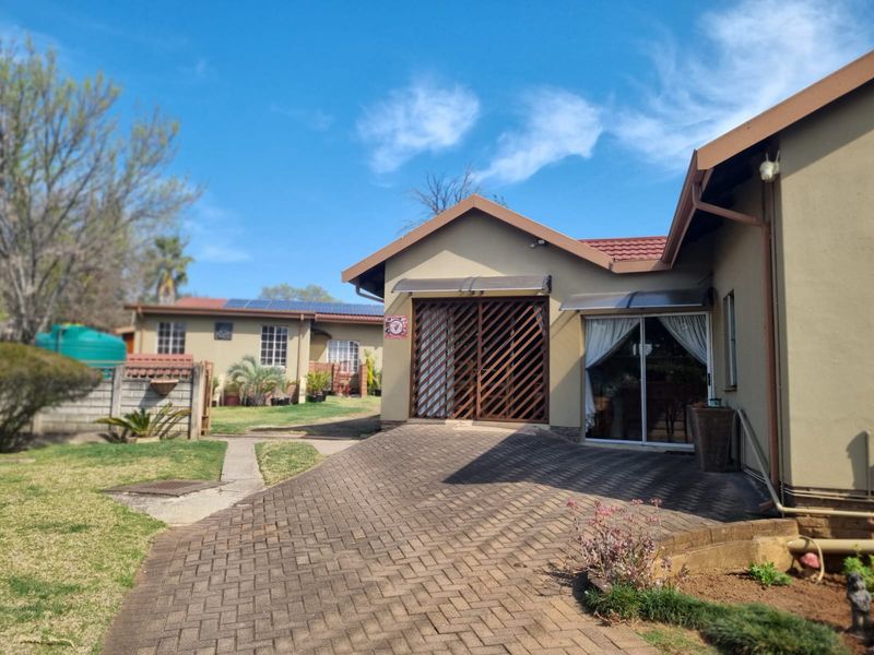 Rear exterior view of the property featuring a paved driveway, sliding glass door access, security gate, and a well-maintained garden area.