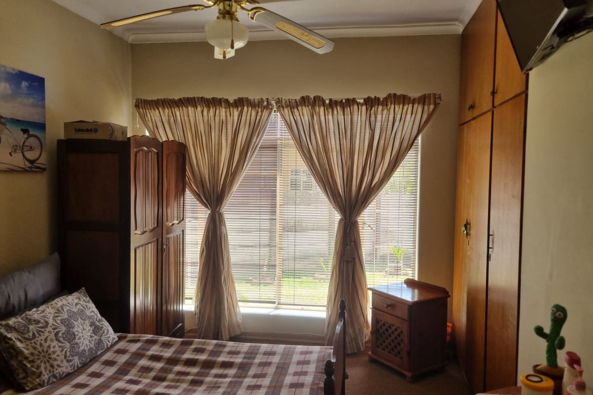 A bedroom featuring built-in wooden cupboards, a ceiling fan, and venetian blinds, offering a functional space with traditional finishes.