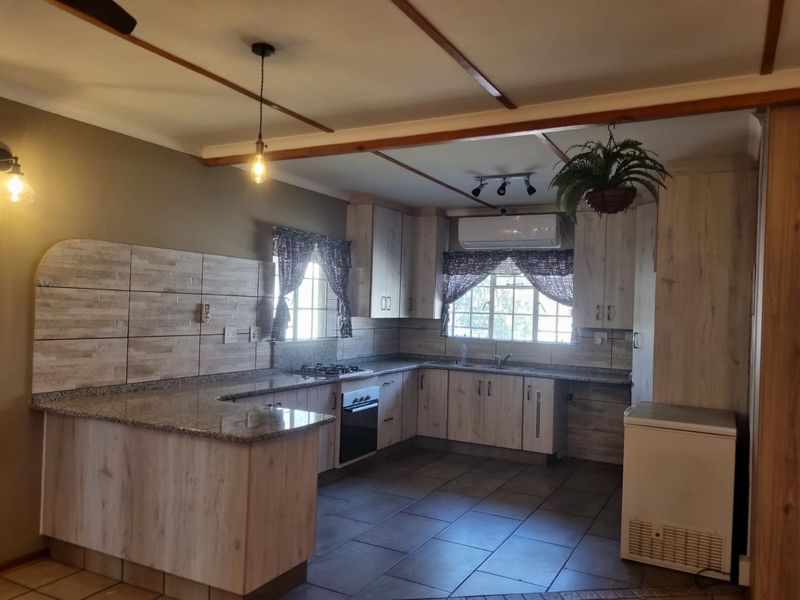 A functional kitchen featuring light wood-finish cabinetry, granite countertops, a gas hob, built-in oven, and tiled flooring with an integrated air conditioning unit.