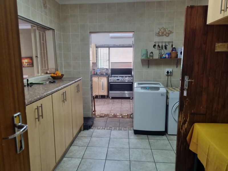 Functional scullery and laundry area featuring tiled finishes, ample cabinetry, and a freestanding gas stove in the adjacent kitchen space.