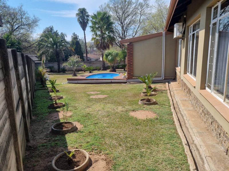 Rear garden featuring a swimming pool, paved surround, and established landscaping, adjacent to the main house structure with stone cladding details.