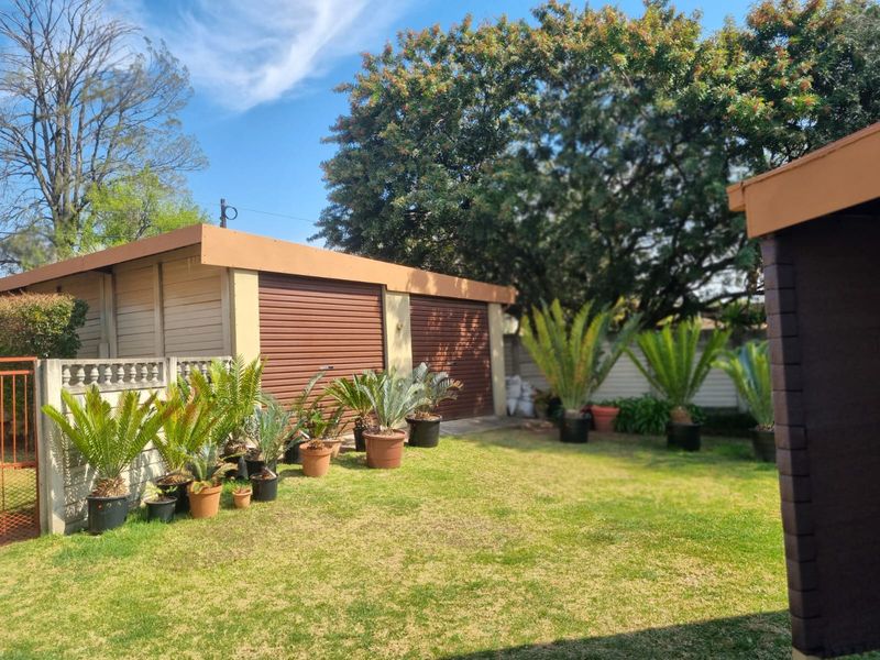 A rear garden view featuring a double garage with roller shutter doors and a well-maintained lawn area.