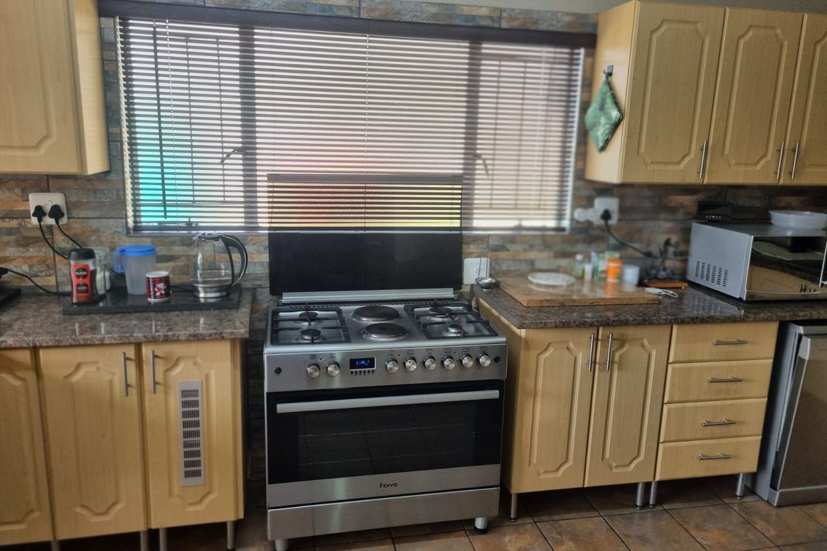 A functional kitchen featuring light wood-finish cabinetry, stone-look countertops, a tiled backsplash, and a stainless steel freestanding gas stove.