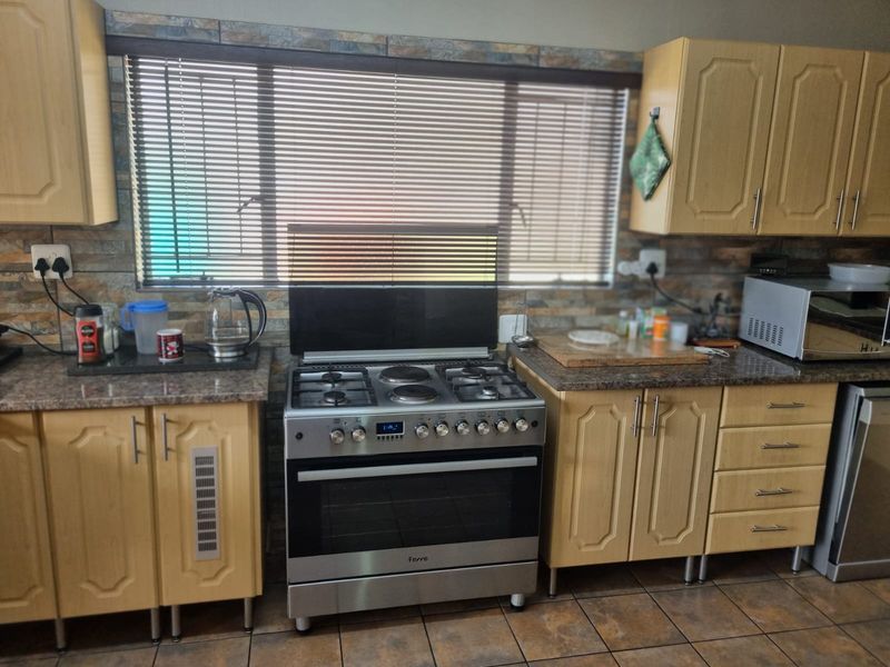A functional kitchen featuring light wood-finish cabinetry, stone-look countertops, a tiled backsplash, and a stainless steel freestanding gas stove.