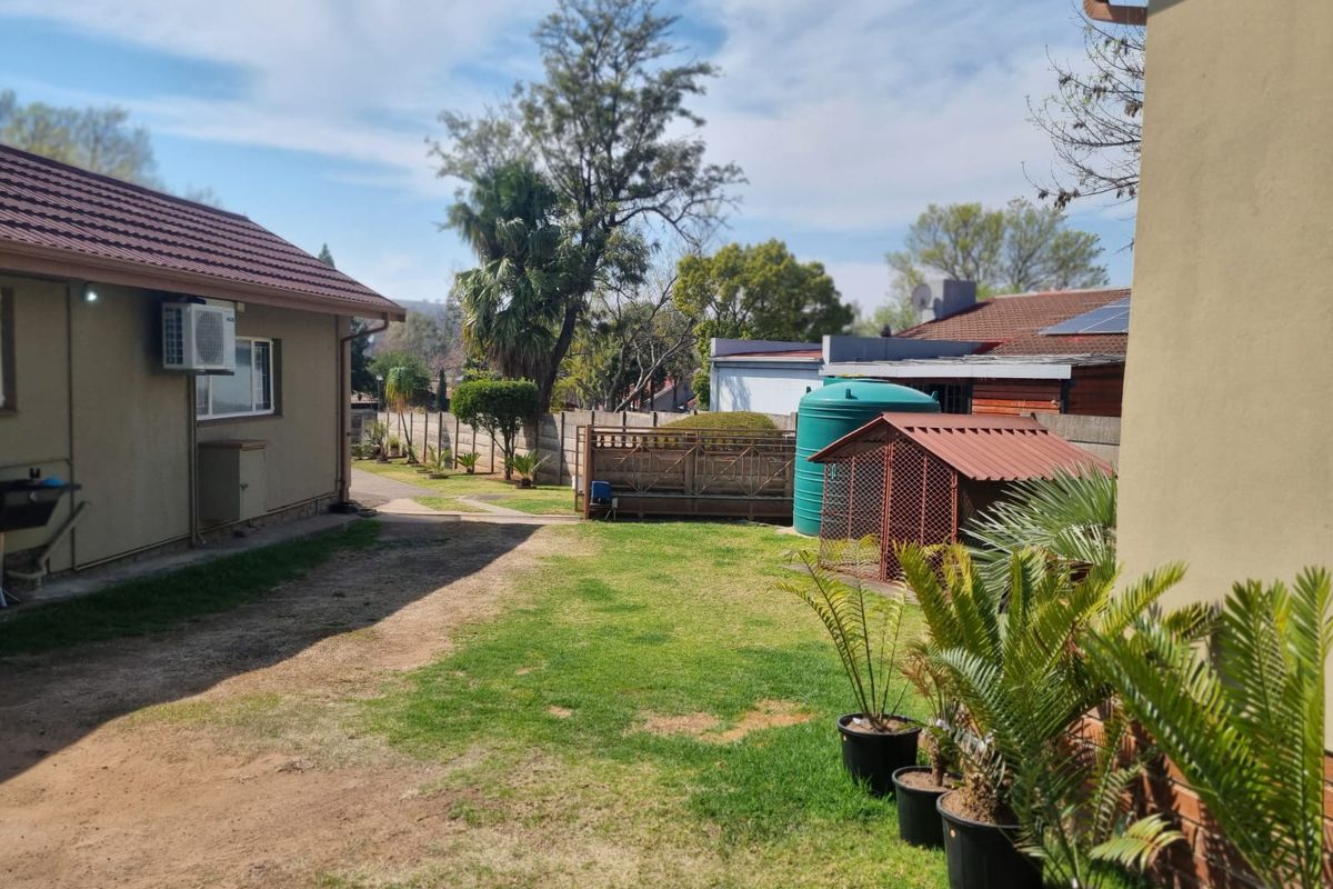 A view of the rear garden area featuring a lawn, paved pathway, water storage tank, and exterior wall-mounted air conditioning unit.