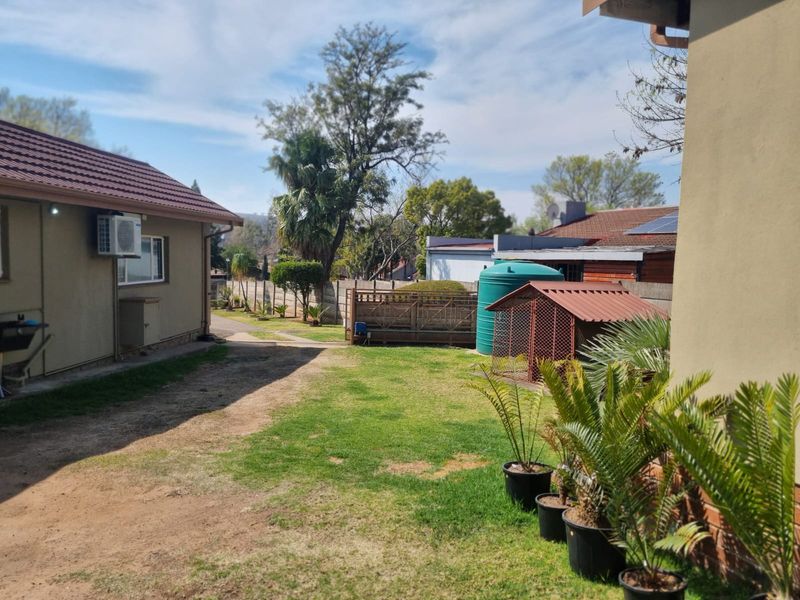A view of the rear garden area featuring a lawn, paved pathway, water storage tank, and exterior wall-mounted air conditioning unit.