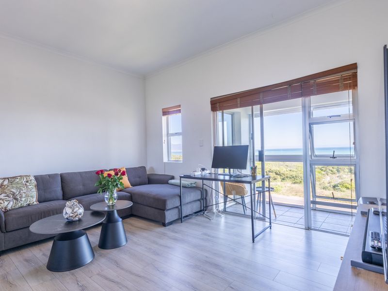 Bright living room featuring light laminate flooring and large sliding glass doors that open to a balcony with scenic coastal views.