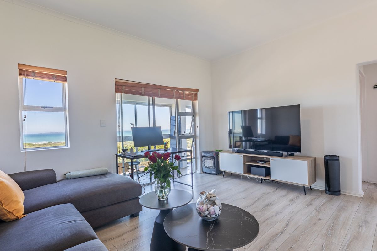 A bright living room featuring light-toned laminate flooring, large windows, and sliding glass doors that offer scenic coastal views.