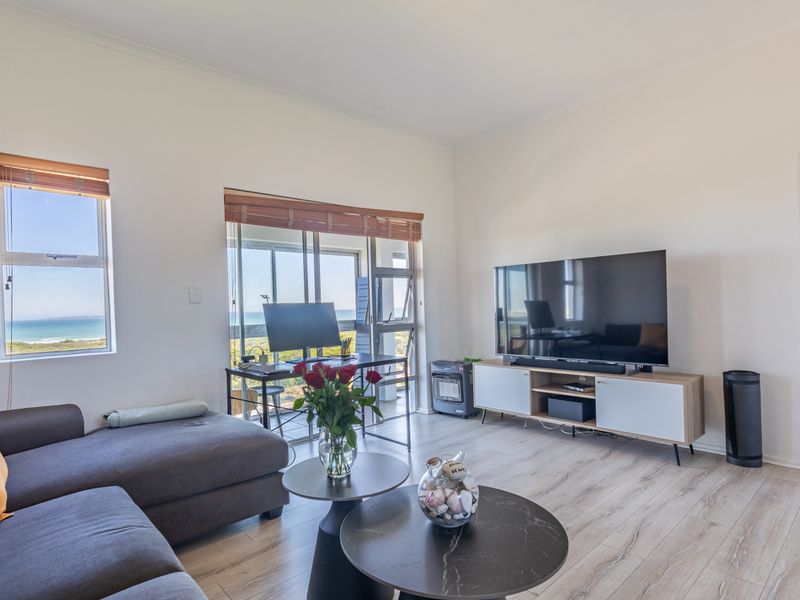 A bright living room featuring light-toned laminate flooring, large windows, and sliding glass doors that offer scenic coastal views.