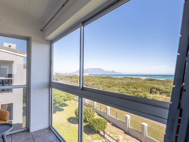 Enclosed balcony featuring large aluminium sliding windows with expansive views of the coastline and Table Mountain.