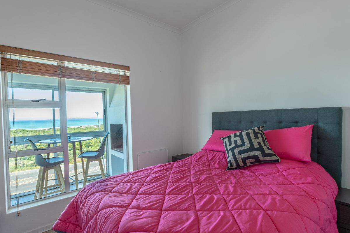 A bright bedroom featuring a sliding glass door with access to a balcony and scenic coastal views.