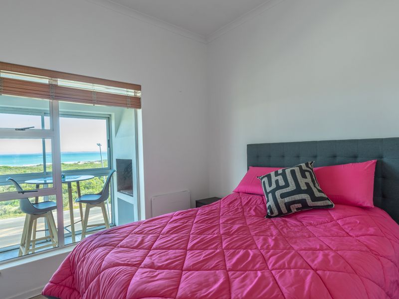 A bright bedroom featuring a sliding glass door with access to a balcony and scenic coastal views.