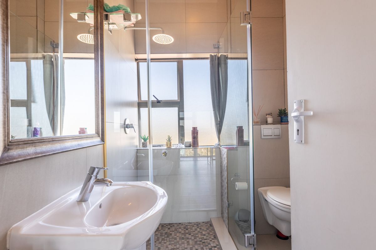 Modern bathroom featuring a wall-mounted basin, glass-enclosed rain shower, and wall-hung toilet with neutral tiling and a large mirror.