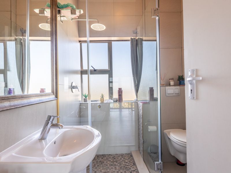 Modern bathroom featuring a wall-mounted basin, glass-enclosed rain shower, and wall-hung toilet with neutral tiling and a large mirror.