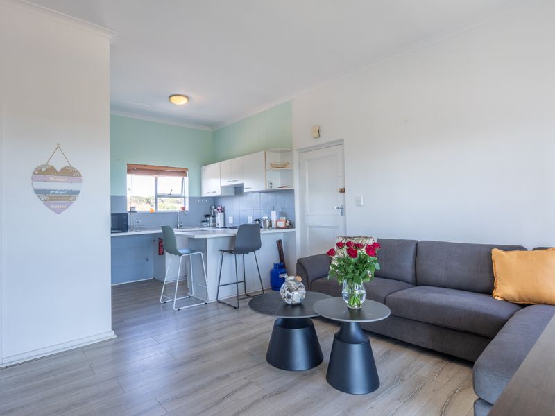 Open-plan living area featuring a functional kitchen with breakfast counter, tiled backsplash, and light-toned laminate flooring throughout the space.