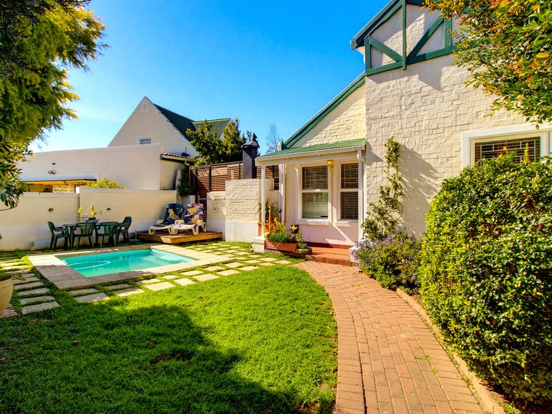 Rear garden area featuring a swimming pool, brick paved pathway, and a well-maintained lawn adjacent to the main house structure.