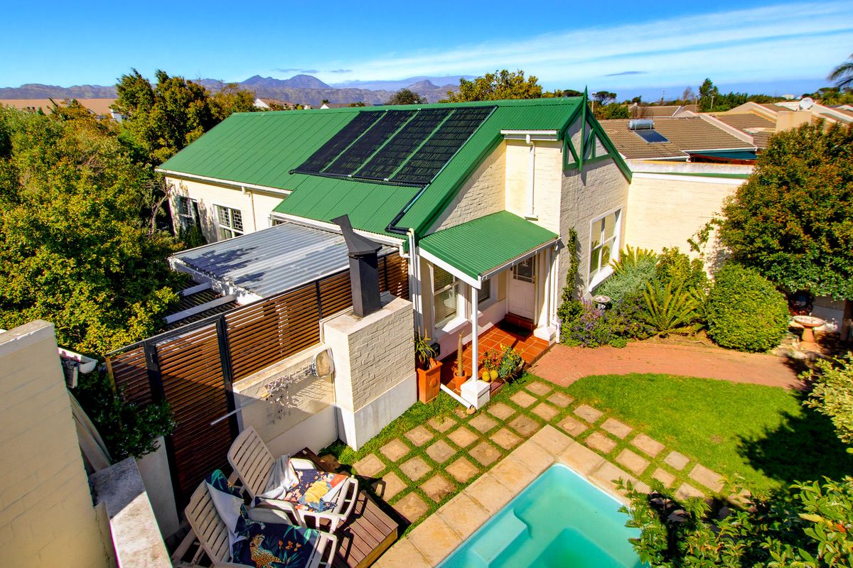 Aerial view of a residential property featuring a green metal roof with solar panels, a swimming pool, and a landscaped garden with outdoor fireplace.