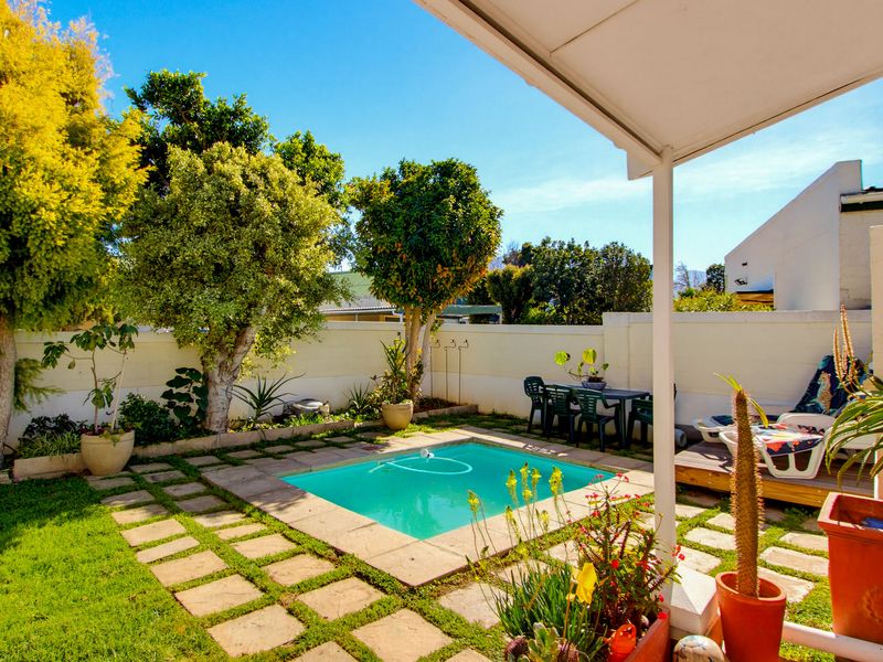 A private outdoor pool area featuring a paved patio, covered seating space, and established garden borders enclosed by a boundary wall.