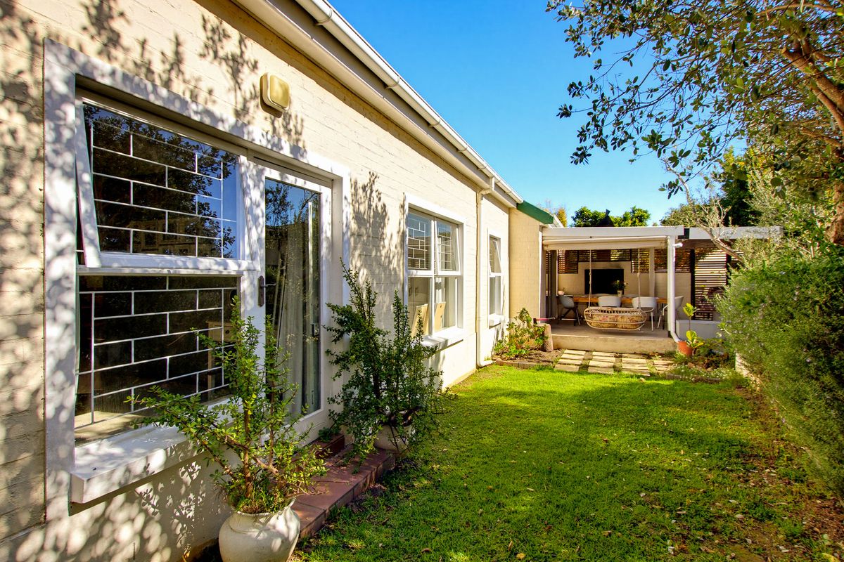 Rear view of the property featuring a well-maintained lawn, security-fitted windows, and a covered patio area suitable for outdoor entertaining.