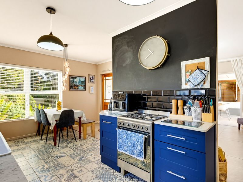 A vibrant kitchen featuring blue cabinetry, a gas stove with a black subway tile backsplash, and decorative patterned floor tiles, adjacent to a dining area.