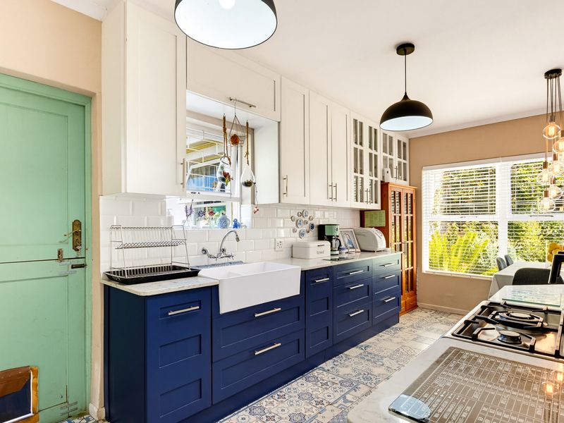 A bright, modern kitchen featuring navy blue lower cabinetry, white upper cabinets, a farmhouse sink, subway tile backsplash, and decorative patterned floor tiles.
