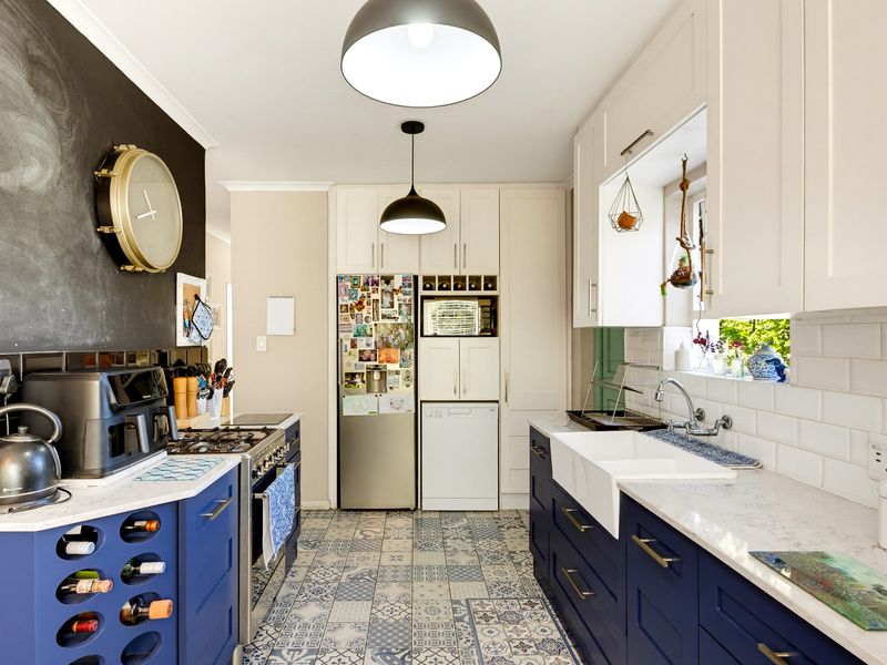 A well-appointed kitchen featuring blue cabinetry, white quartz countertops, a farmhouse sink, subway tile backsplash, and integrated wine storage.