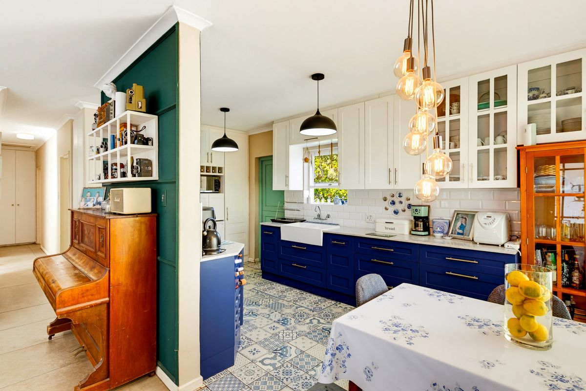A well-maintained kitchen featuring blue lower cabinetry, white upper cabinets, a farmhouse sink, subway tile backsplash, and decorative patterned floor tiles.