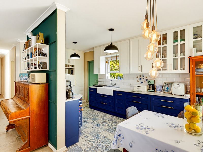 A well-maintained kitchen featuring blue lower cabinetry, white upper cabinets, a farmhouse sink, subway tile backsplash, and decorative patterned floor tiles.