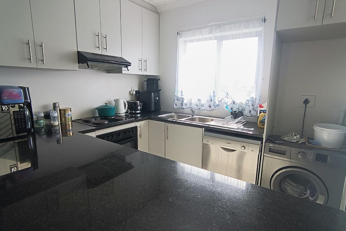 Functional kitchen featuring granite countertops, ample cabinetry, built-in oven and hob, extractor fan, and integrated dishwasher with dedicated laundry appliance space.