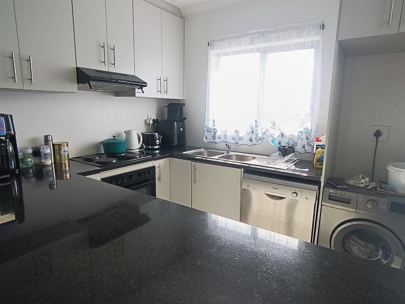Functional kitchen featuring granite countertops, ample cabinetry, built-in oven and hob, extractor fan, and integrated dishwasher with dedicated laundry appliance space.